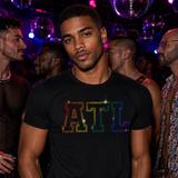 Man wearing a fitted black T-shirt with bold rainbow rhinestone "ATL" lettering at a gay nightclub. Atlanta Pride LGBTQ+ graphic tee for Pride festivals, nightlife, circuit parties, travel, and everyday statement fashion by Rico Starr
