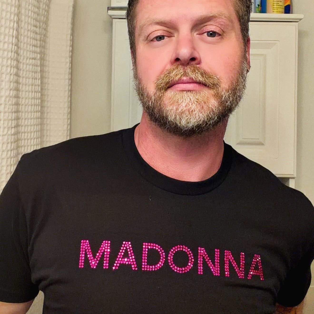 Man wearing a black t-shirt with 'MADONNA' in pink rhinestone letters by Rico Starr