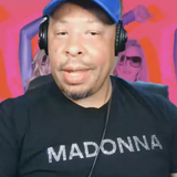 Man wearing black rhinestone "Madonna" graphic t-shirt with headphones and baseball cap on a livestream by Rico Starr
