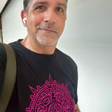 Man wearing a black t-shirt featuring a vibrant pink rhinestone Aztec calendar design inspired by Mexican heritage and culture. Bold statement  style, nightlife energy and sparkling rhinestone detailing by Rico Starr