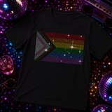 A black short-sleeve t-shirt featuring a rhinestone Progress Pride Flag graphic by Rico Starr