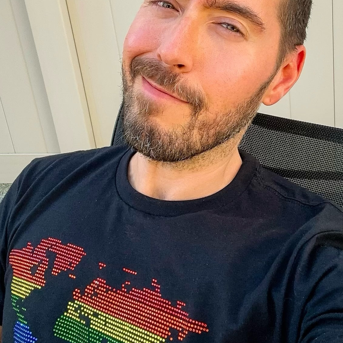 Man wearing a black t-shirt featuring a rhinestone rainbow world map graphic. LGBTQ+ Pride apparel celebrating queer visibility, equality, and community with vibrant rainbow colors and sparkling rhinestone details by Rico Starr