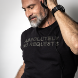Male DJ wearing a black rhinestone “Absolutely No Requests” t-shirt while listening to music through headphones by Rico Starr