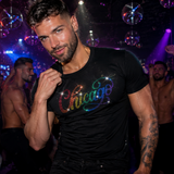 Male model wearing a fitted black t-shirt featuring a rainbow rhinestone “Chicago” script design inspired by LGBTQ Pride, disco fashion, and nightlife culture by Rico Starr
