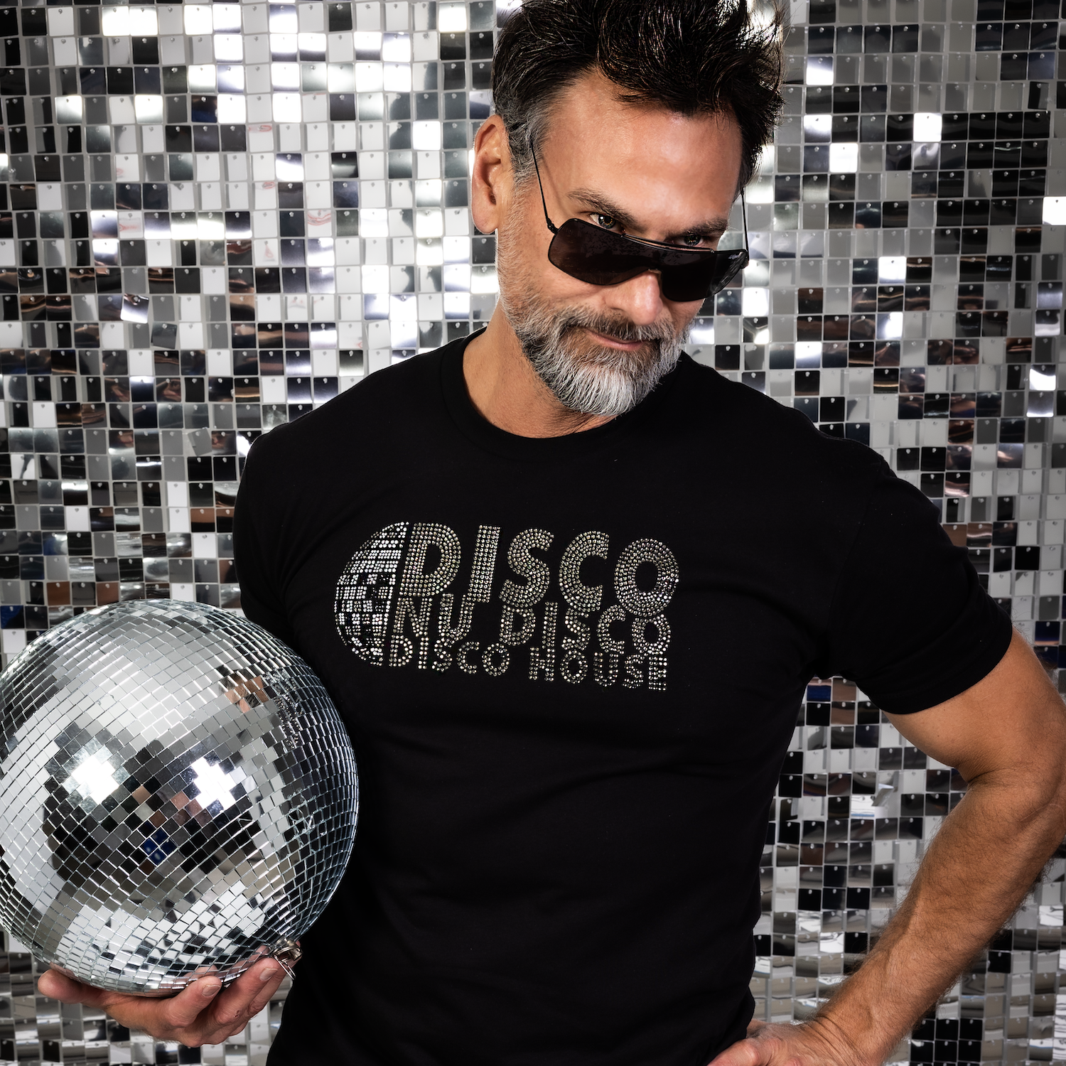Male model wearing a fitted black rhinestone “Disco Nu Disco Disco House” t-shirt while holding a disco ball in front of a mirrored disco tile backdrop by Rico Starr