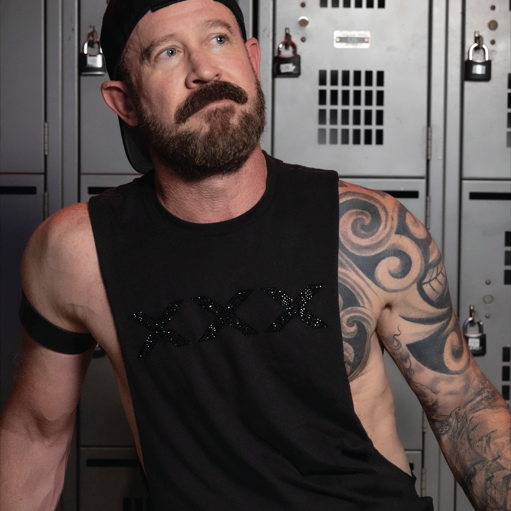 Man wearing a black deep armhole tank top featuring a black rhinestone XXX graphic. Bold LGBTQ+ nightlife fashion with a sleek monochromatic design, modern athletic fit, and sexy clubwear styling for gay men, Pride events, parties, festivals, and nightlife culture by Rico Starr