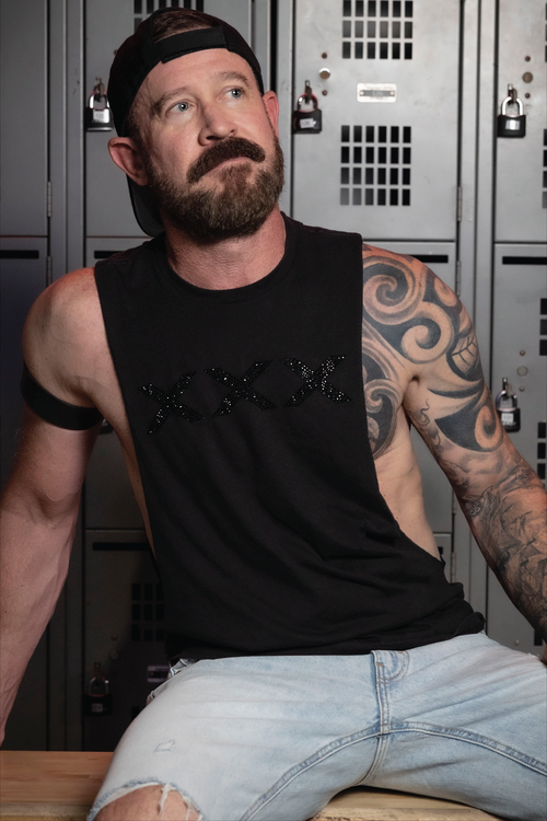 Man wearing a black deep armhole tank top featuring a black rhinestone XXX graphic. Bold LGBTQ+ nightlife fashion with a sleek monochromatic design, modern athletic fit, and sexy clubwear styling for gay men, Pride events, parties, festivals, and nightlife culture by Rico Starr